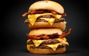 A double bacon cheeseburger with melted american cheese and crispy bacon, stacked high on a black background.