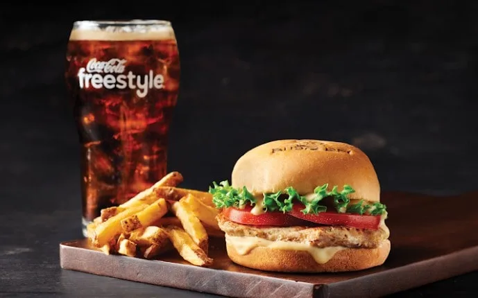 A close-up of a juicy burger with the best beef with a glass of soda.
