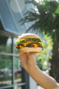 A hand holding up a BurgerFi burger with a juicy patty, lettuce, and cheese.